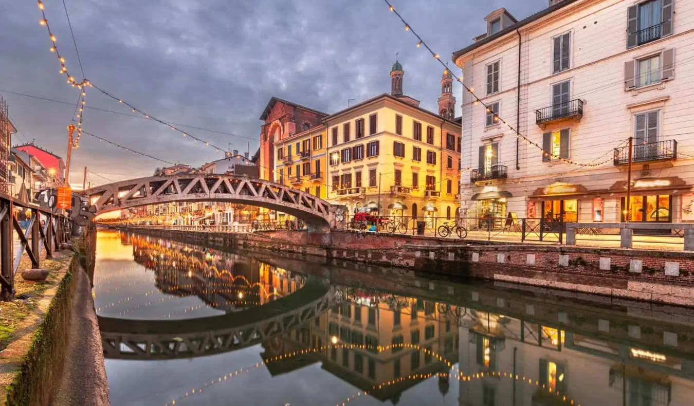 Terusan yang indah dan bersejarah di kejiranan Navigli dengan lampu bertali digantung di atasnya pada waktu senja di Milan, Itali