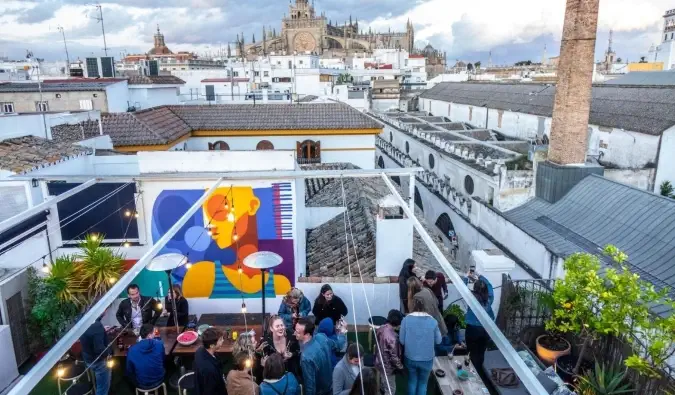 Gent de festa al terrat de La Banda Rooftop Hostel amb l'horitzó de Sevilla, Espanya al fons