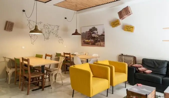 Eclectische gemeenschappelijke ruimte van The Nomad Hostel met houten tafels en felgele loungestoelen in Sevilla, Spanje