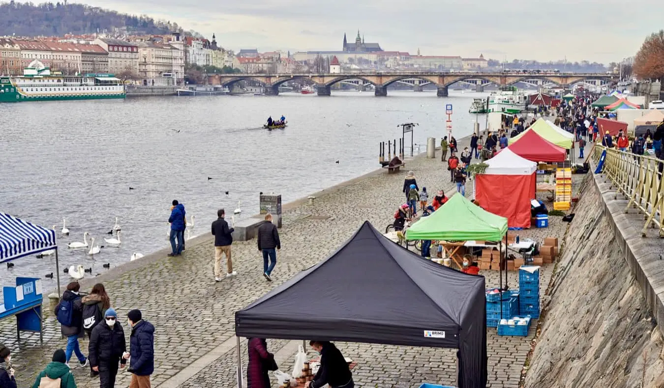 Orang-orang berjalan di dekat kios-kios di sepanjang sungai di Praha, Czechia