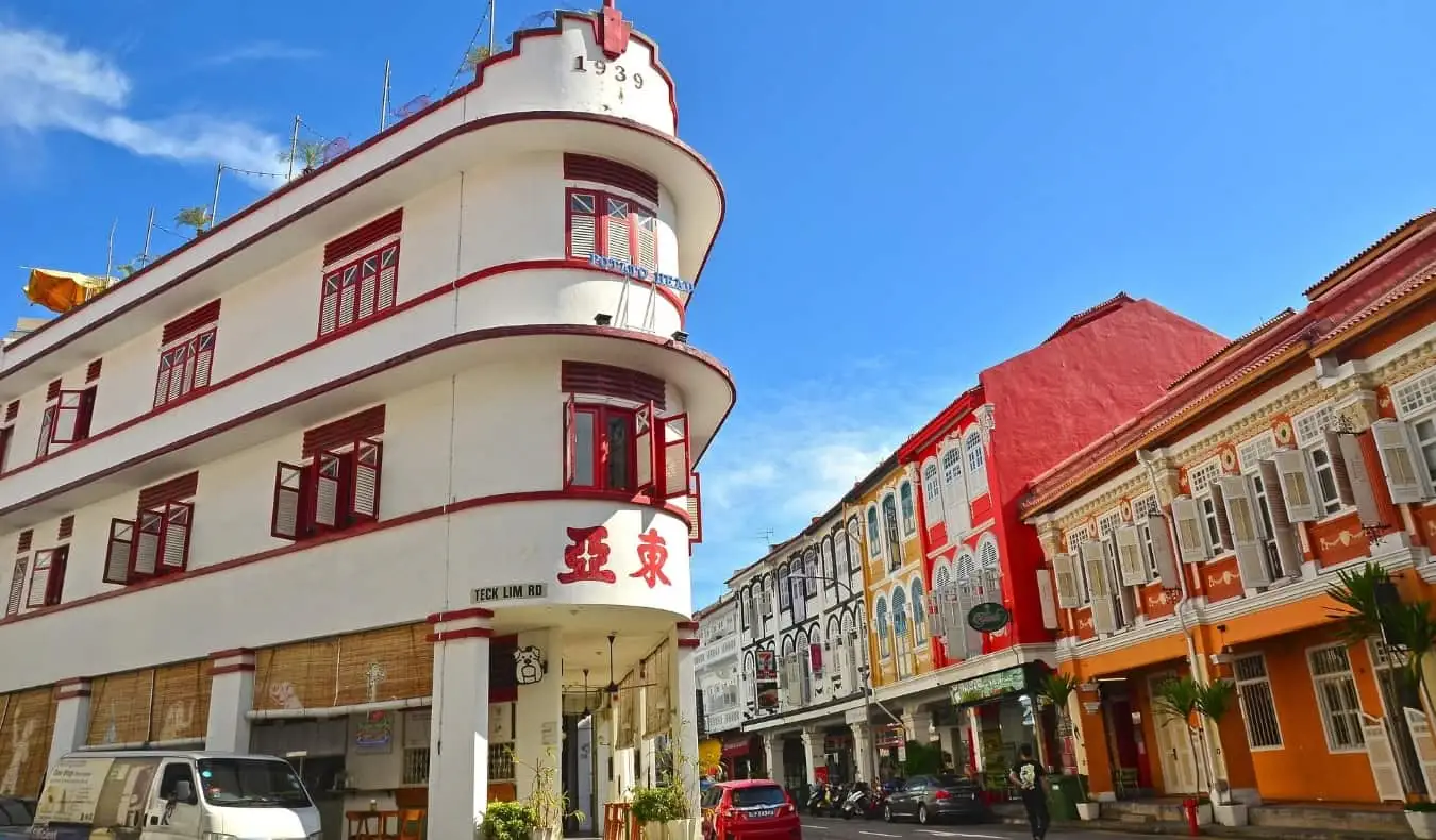 En trekantet hvit bygning trimmet med rødt og dekorert med kinesiske tegn, på en gate med andre fargerike bygninger i Chinatown, Singapore