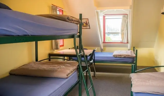 Mga simpleng metal na bunk bed sa isang maaraw na dilaw na silid sa Southern Laughter Backpackers hostel sa Queenstown, New Zealand