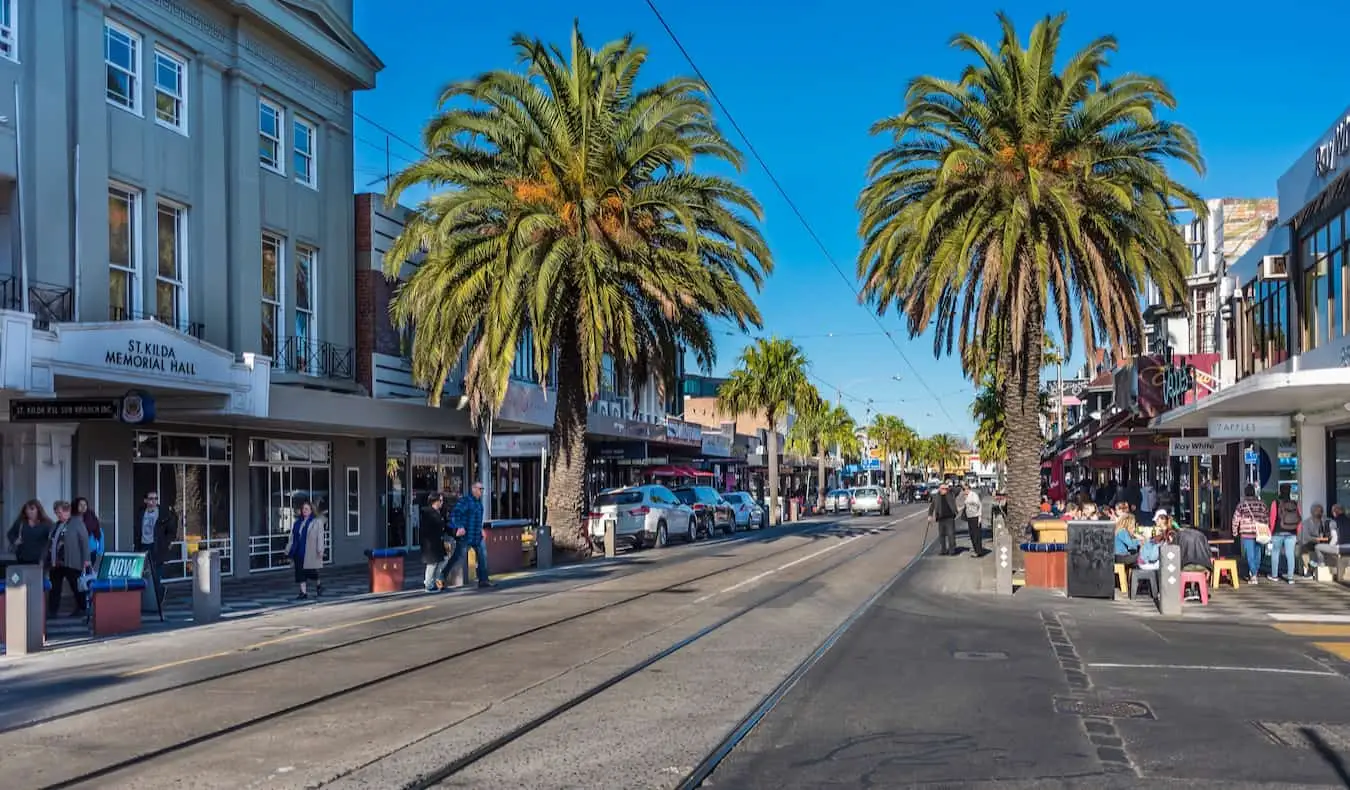 Menschen entspannen sich an einem hellen und sonnigen Tag auf einer Straße in St. Kilda, Melbourne