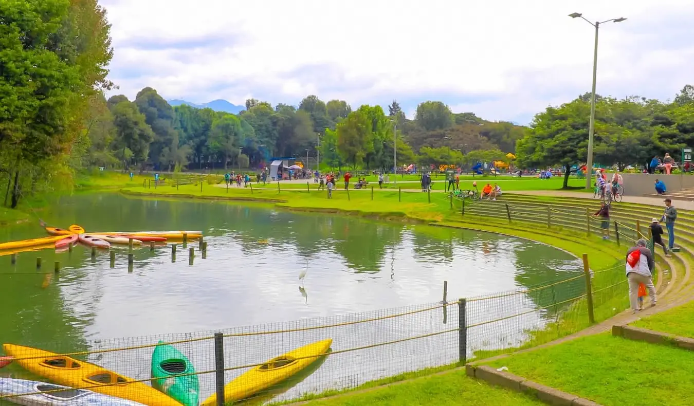 Caiaques flutuando em um lago, cercados por pessoas caminhando e correndo, no Parque Simon Bolívar, em Bogotá, Colômbia