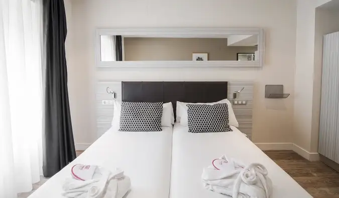 Un miroir est suspendu au-dessus d'un lit double avec des draps blancs et des serviettes de bain disposés de manière décorative à l'hôtel Petit Palace Puerta del Sol à Madrid, Espagne