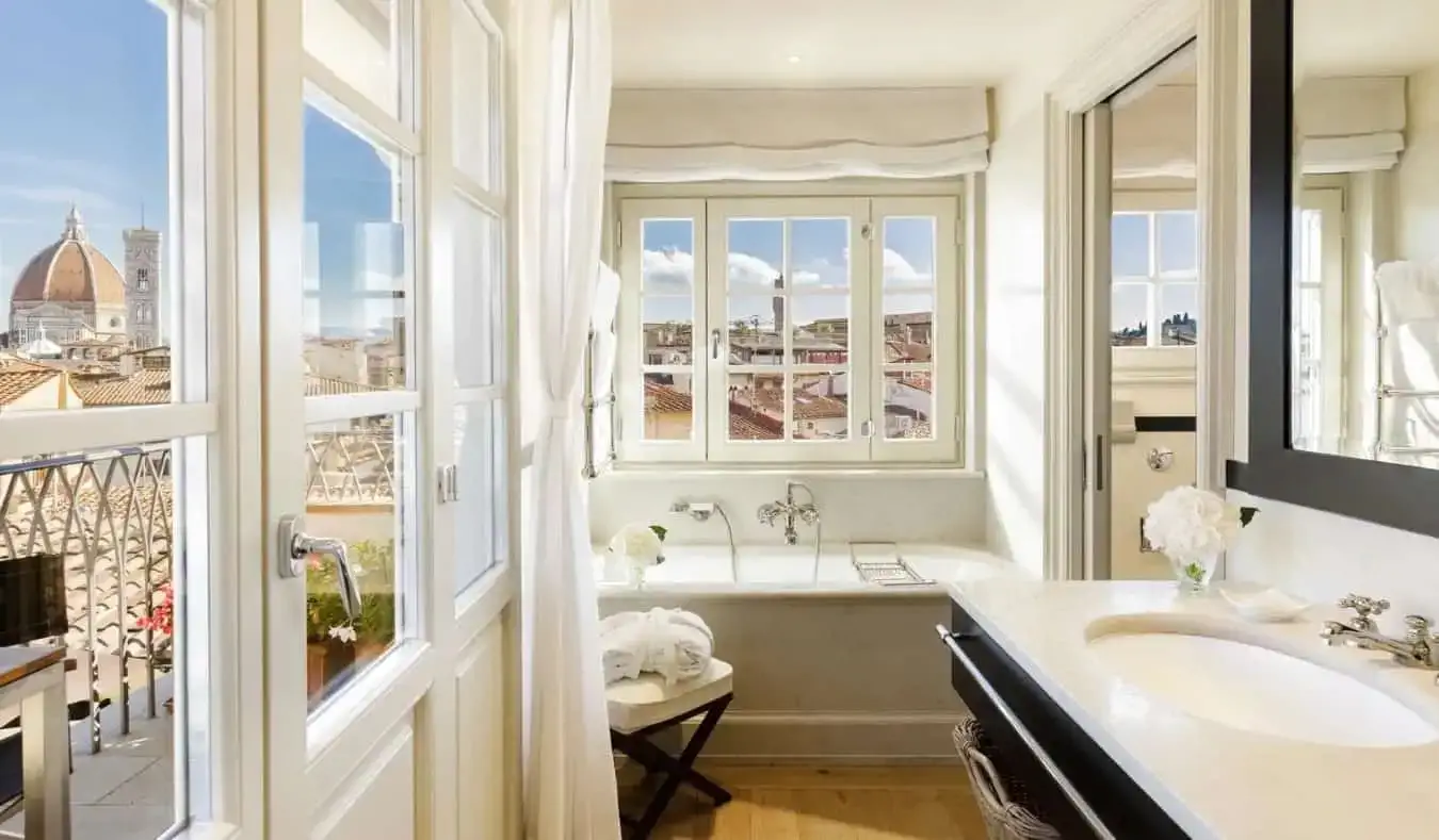 Un lujoso baño lleno de una gran bañera, pisos de madera y ventanas con vista al Duomo desde una de ellas en The Place, un hotel de cinco estrellas en Florencia, Italia.