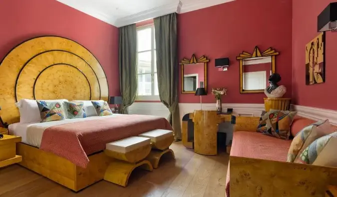 Um quarto de hotel com paredes vibrantes em cor salmão, cama, mesa e espelhos, tudo em estilo Art Déco de madeira no La Maison du Sage, um hotel em Florença, Itália