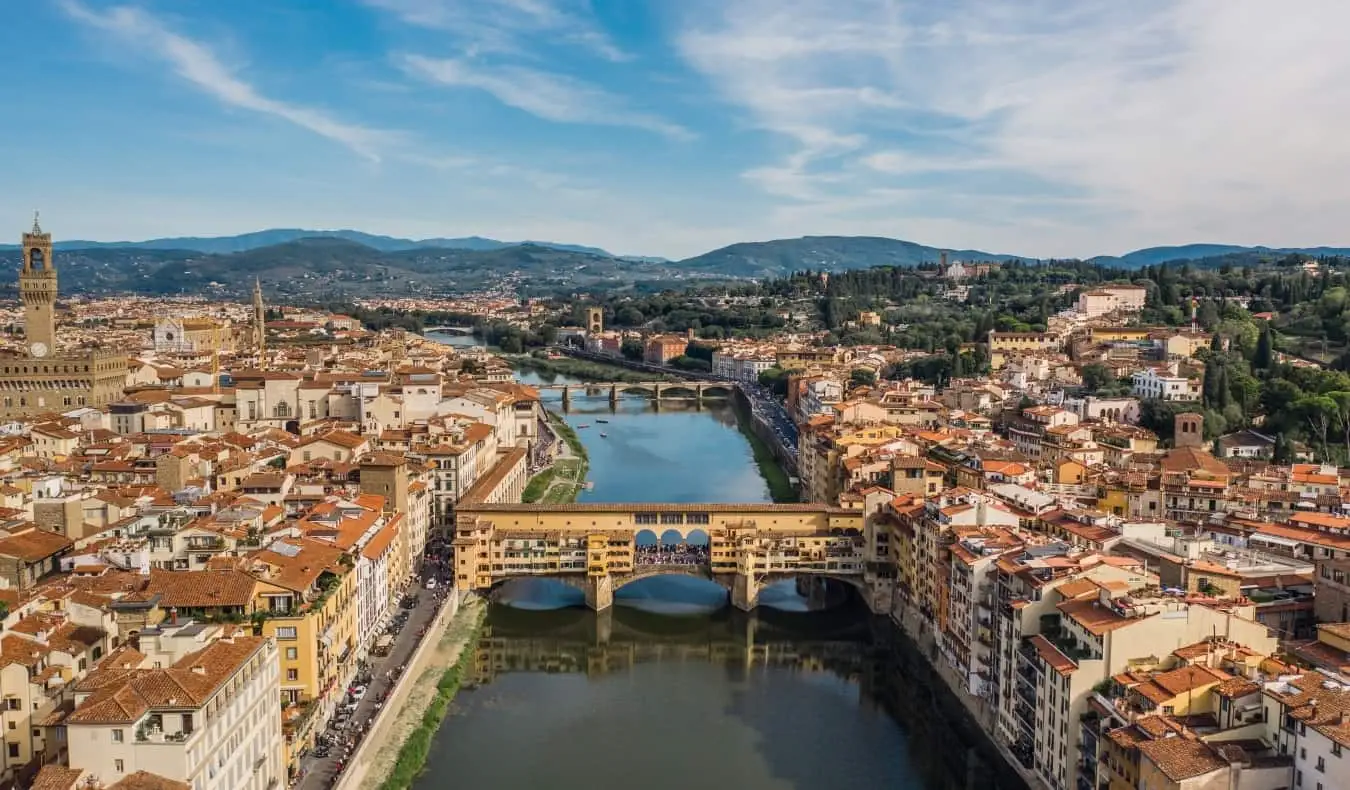 Ilmakuva Firenzen kaupungista, jonka läpi virtaa Arno-joki, Ponte Vecchio etualalla ja vuoret taustalla