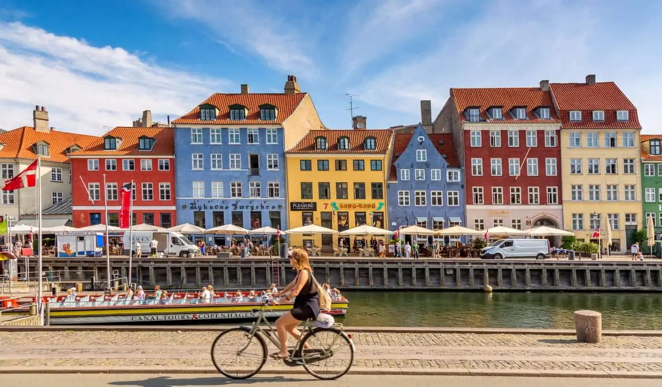 En kvinde, der cykler forbi farverige, historiske bygninger langs en kanal i Indry By, det historiske centrum af København, Danmark