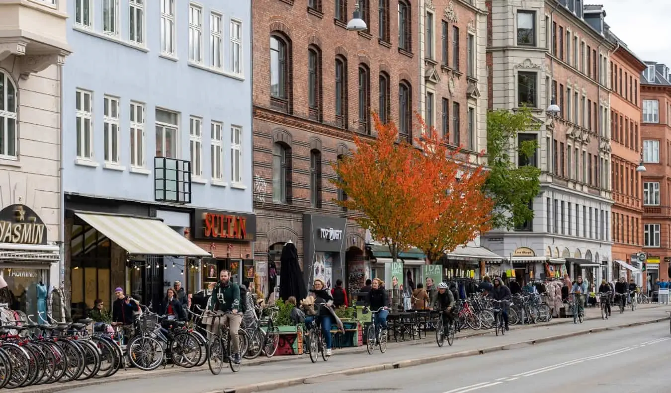 Menschen radeln eine von Restaurants gesäumte Straße im Stadtteil Nørrebro in Kopenhagen, Dänemark, entlang