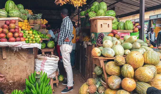 Un hombre en Ruanda parado en un supermercado rodeado de fruta fresca.