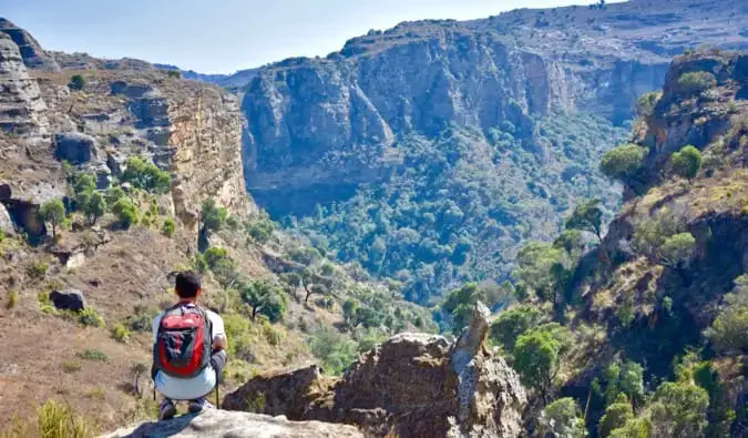 Il nomade Matt accovacciato su una scogliera, guarda in lontananza le colline e le scogliere