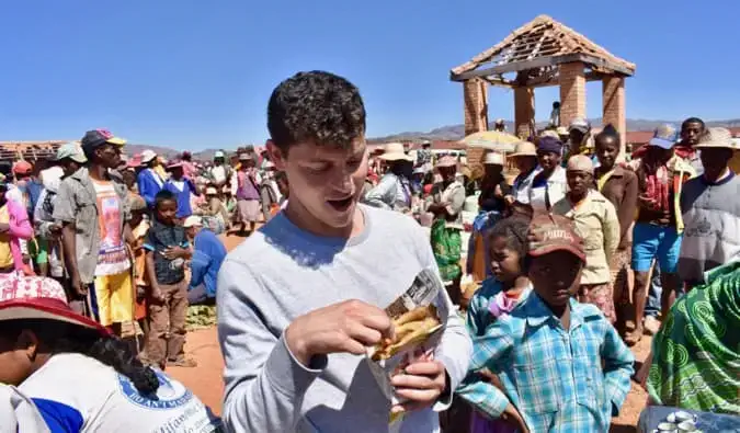 Nomadisks Mets ēd ielas ēdienu rosīgā Madagaskaras tirgū