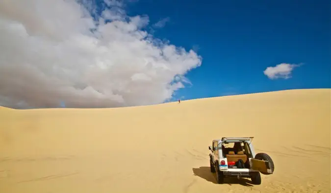 Un coche alquilado explorando las dunas de arena de África bajo un cielo azul brillante