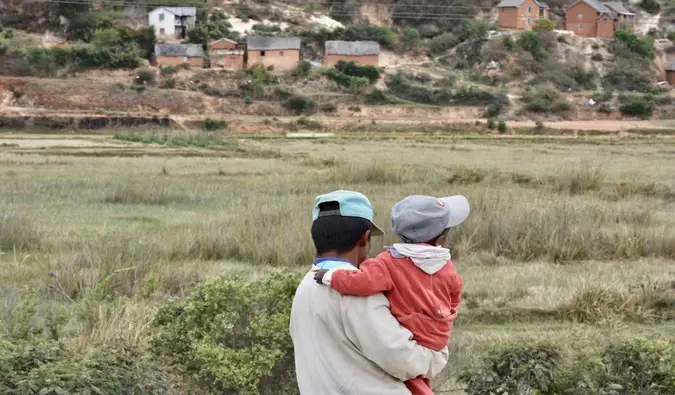 Ein Vater trägt seinen kleinen Sohn auf einem Feld in Madagaskar