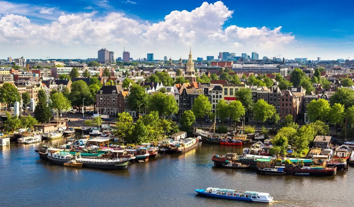 Panoramablick auf die Skyline von Amsterdam mit angedockten und an einem Fluss schwimmenden Booten im Vordergrund