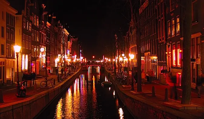 Een gracht die door de rosse buurt van Amsterdam loopt, 's nachts verlicht met rode lichten.