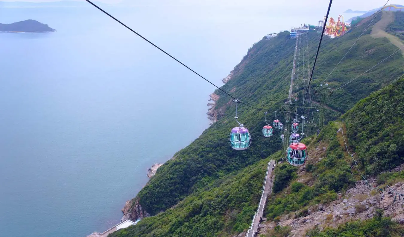 Ngong Ping 360 trošu vagoniņš ar skatu uz ūdeni un zaļajiem kalniem lejā Honkongā