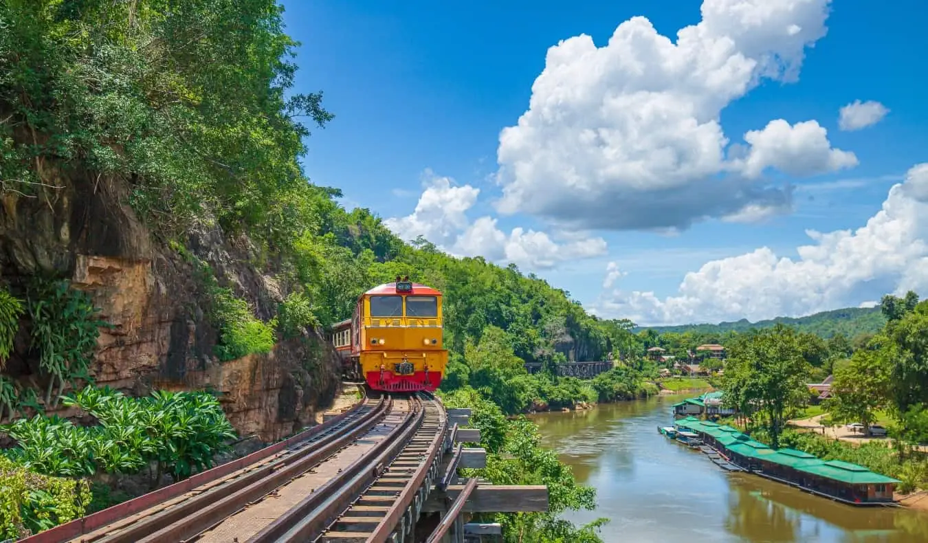 et tog, der krammer klippesiden i Kanchanaburi, Thailand med på en solskinsdag med smuk udsigt over Kwai Noi-floden til højre