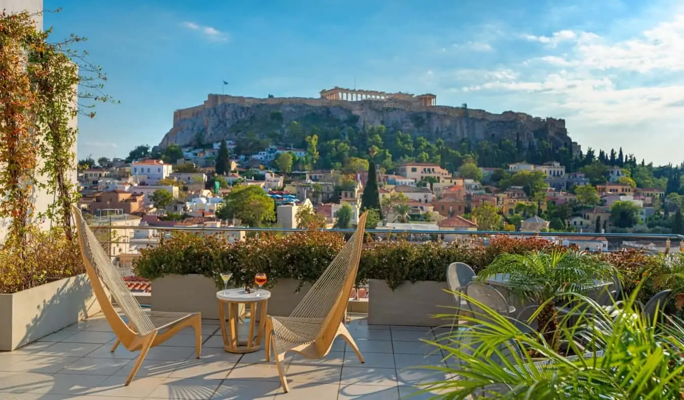 Chaises longues en bois devant une table basse avec verre de champagne dessus sur le toit-terrasse de l'hôtel Plaka surplombant l'Acropole à Athènes, Grèce