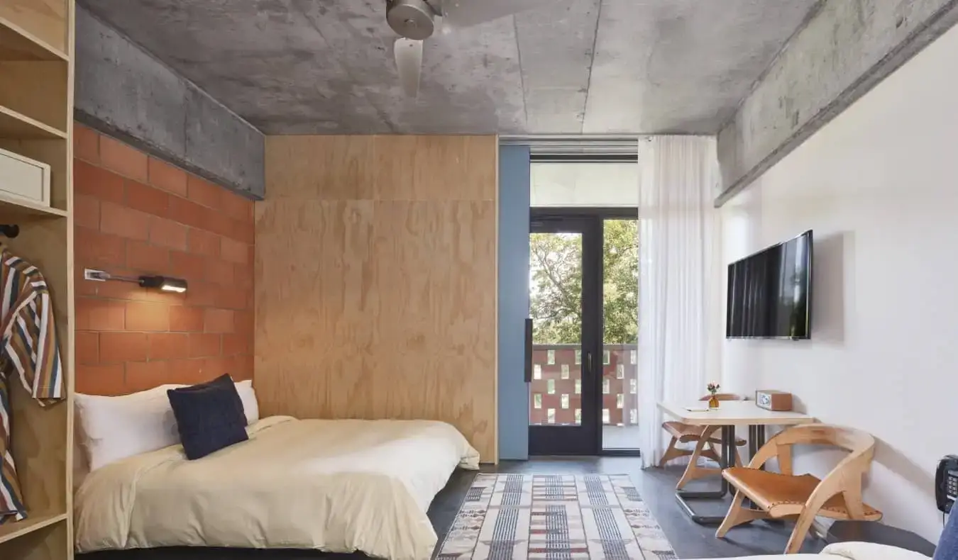 Gastenkamer met een bakstenen muur, terras en houten bureau in The Carpenter Hotel in Austin, Texas