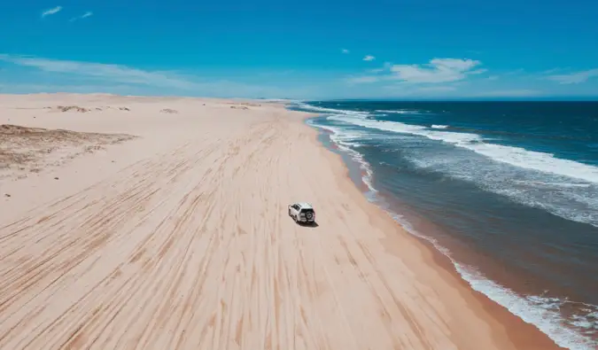 Une grande plage ouverte en Australie avec un véhicule 4x4 roulant dans le sable