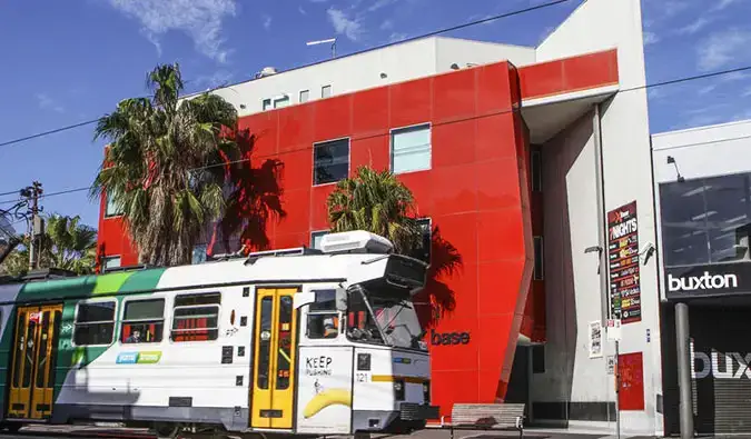 Rødt eksteriør av Base St. Kilda hostel med trikk som går forbi i Melbourne, Australia