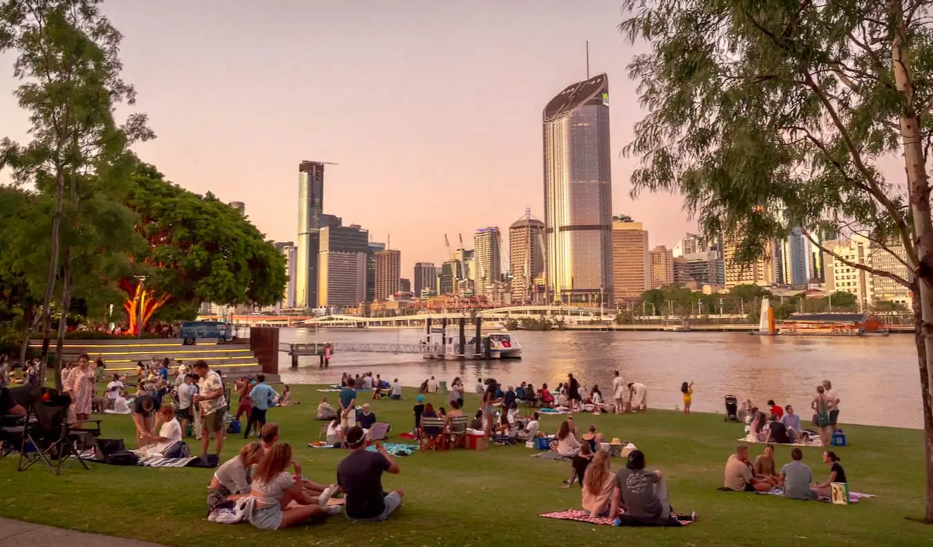 Ludzie relaksujący się na skraju South Bank w pobliżu wody, patrząc na CBD w Brisbane w Australii