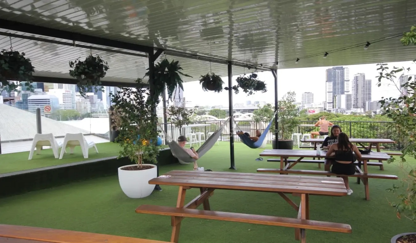 Rooftop terrace na may mga picnic table at mga taong nakatambay sa mga duyan sa City Backpackers sa Brisbane, Australia.