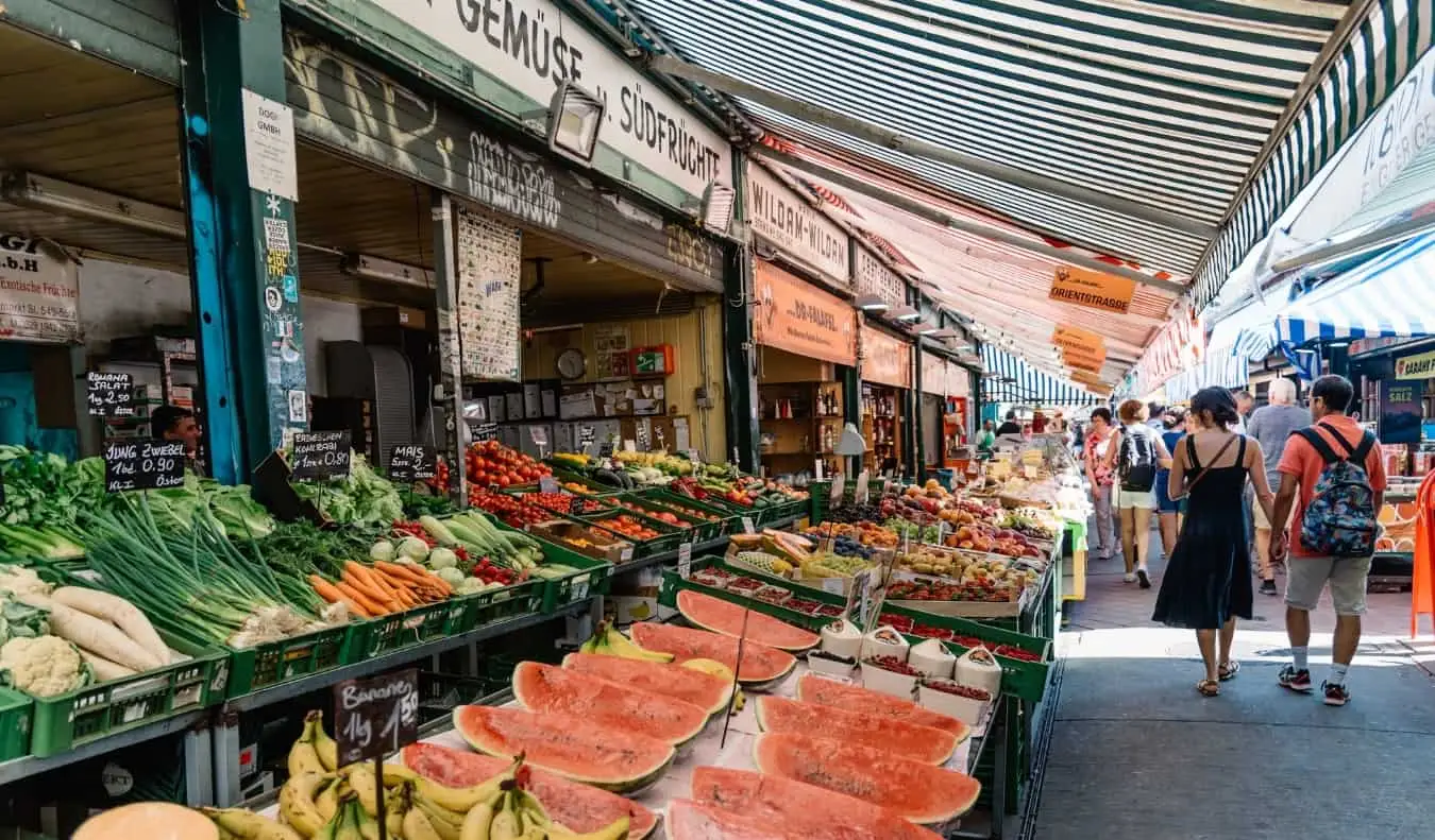 Orang-orang berjalan menyusuri lorong produk di Naschmarkt, dan pasar luar ruangan di Wina, Austria