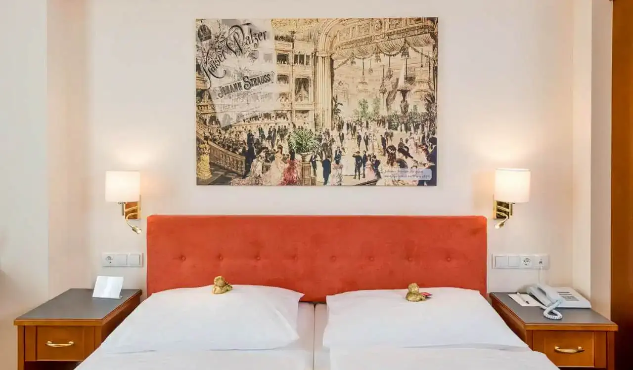 Ein großes, bequemes Bett mit Kunstwerken darüber im Hotel Johann Strauss in Wien, Österreich