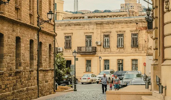 penduduk setempat berjalan-jalan di Baku, Azerbaijan dengan bangunan-bangunan tua berpasir di sekelilingnya