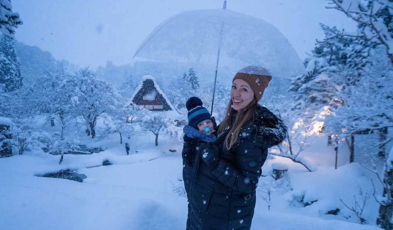 Blogger Kristin Addis fra Be My Travel Muse med sin spæde søn i en bæresele, mens de står i et sneklædt landskab i Japan