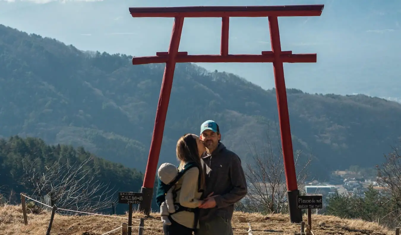 A blogueira Kristin Addis do Be My Travel Muse com seu parceiro e bebê sob um arco torii no Japão