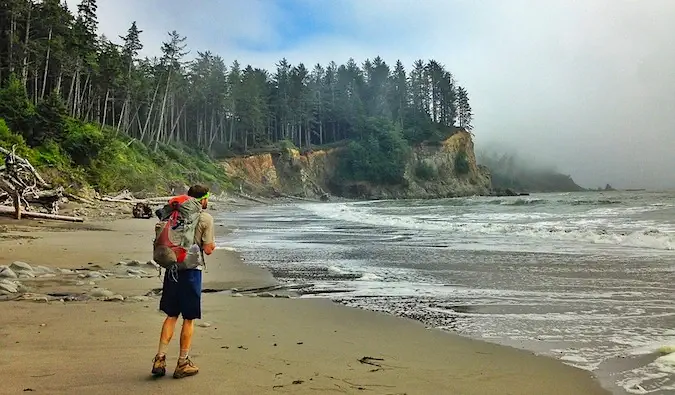 un routard en randonnée sur une plage isolée entourée d'arbres