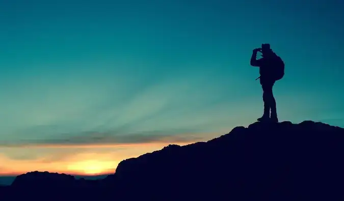 la silhouette d'un routard debout sur une falaise au coucher du soleil