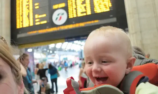 Sohn in einer Babytrage posiert auf einem Bahnhof in Europa