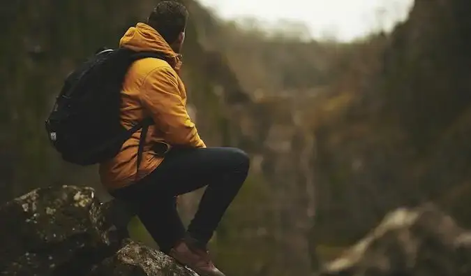 Isang solong hiker na nakasuot ng dilaw na jacket na nakaupo sa kabundukan na nakatingin sa mga tanawin sa paligid niya