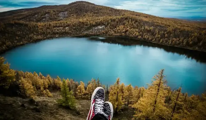 keliautojas, sėdintis ant kalvos su vaizdu į ežerą