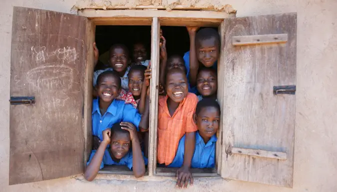 Kanak-kanak sekolah yang tersenyum di Afrika melihat ke luar tingkap bilik darjah