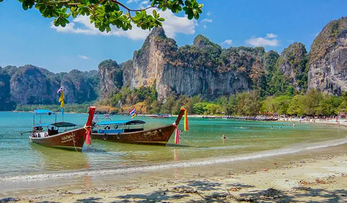 Røde longtail-båter trakk opp til en pittoresk strand med klipper i bakgrunnen, i Thailand