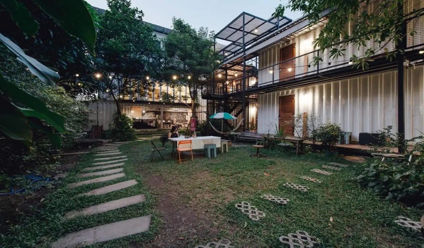 Yard Hostel Bangkok'un geniş, yemyeşil arka bahçesi ve nakliye konteynırları.