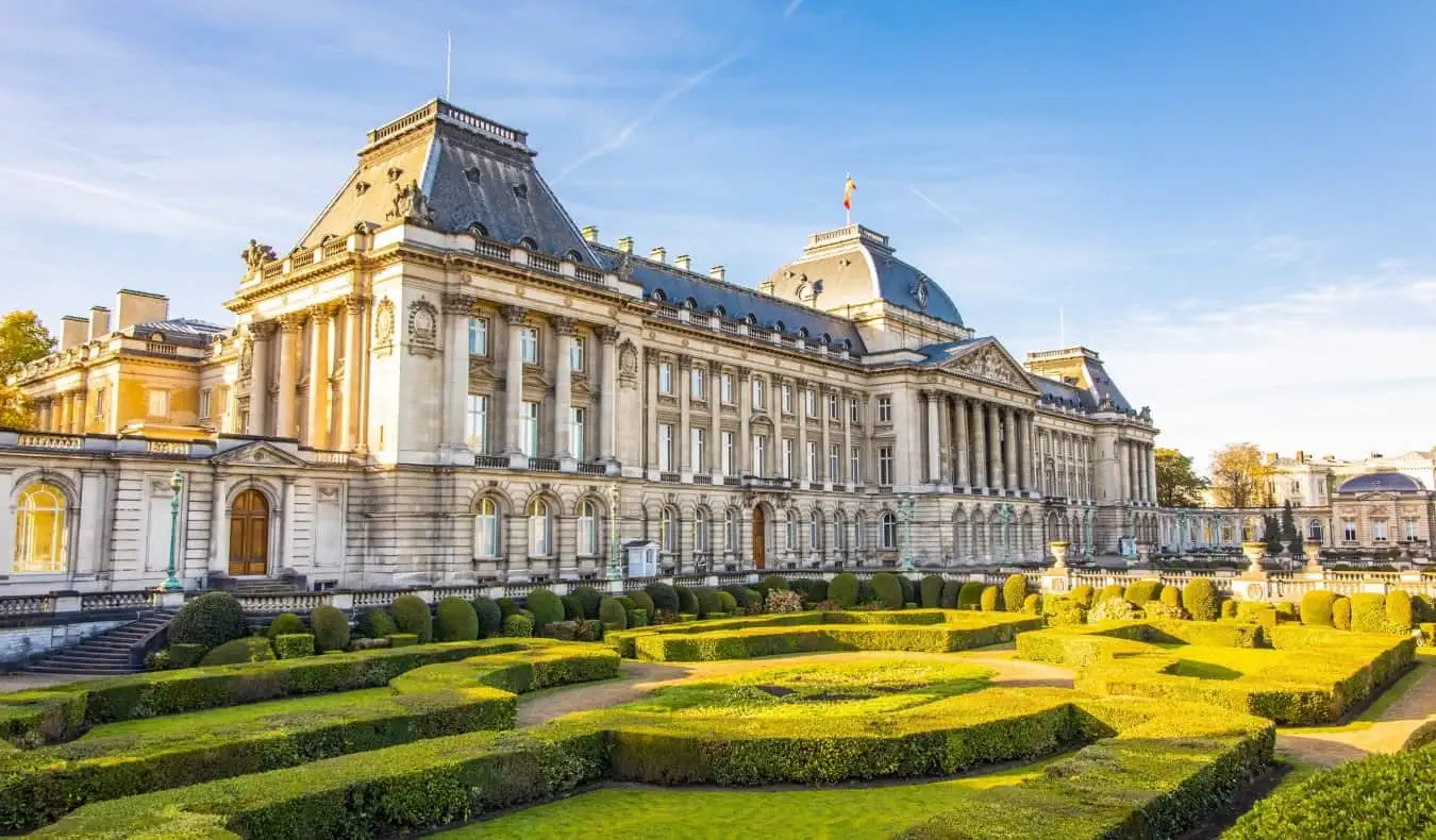 Eksterior megah Istana Kerajaan di Brussels, Belgia, dengan taman terawat di depannya pada hari yang cerah