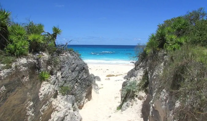 Sandiger Eingang zum karibischen Strand, flankiert von zwei großen grasbewachsenen Felsen