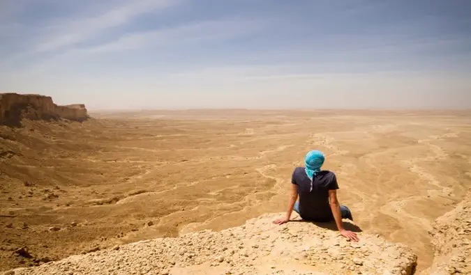 Un viaggiatore solitario seduto su una scogliera nel deserto dell'Arabia Saudita