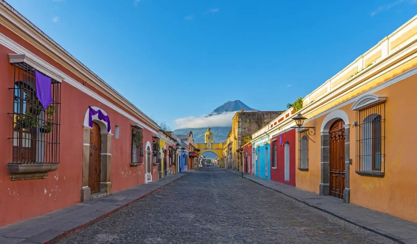 Paisaje urbano de Antigua, Guatemala con casas de colores brillantes y una montaña que se eleva a través de las nubes en el fondo