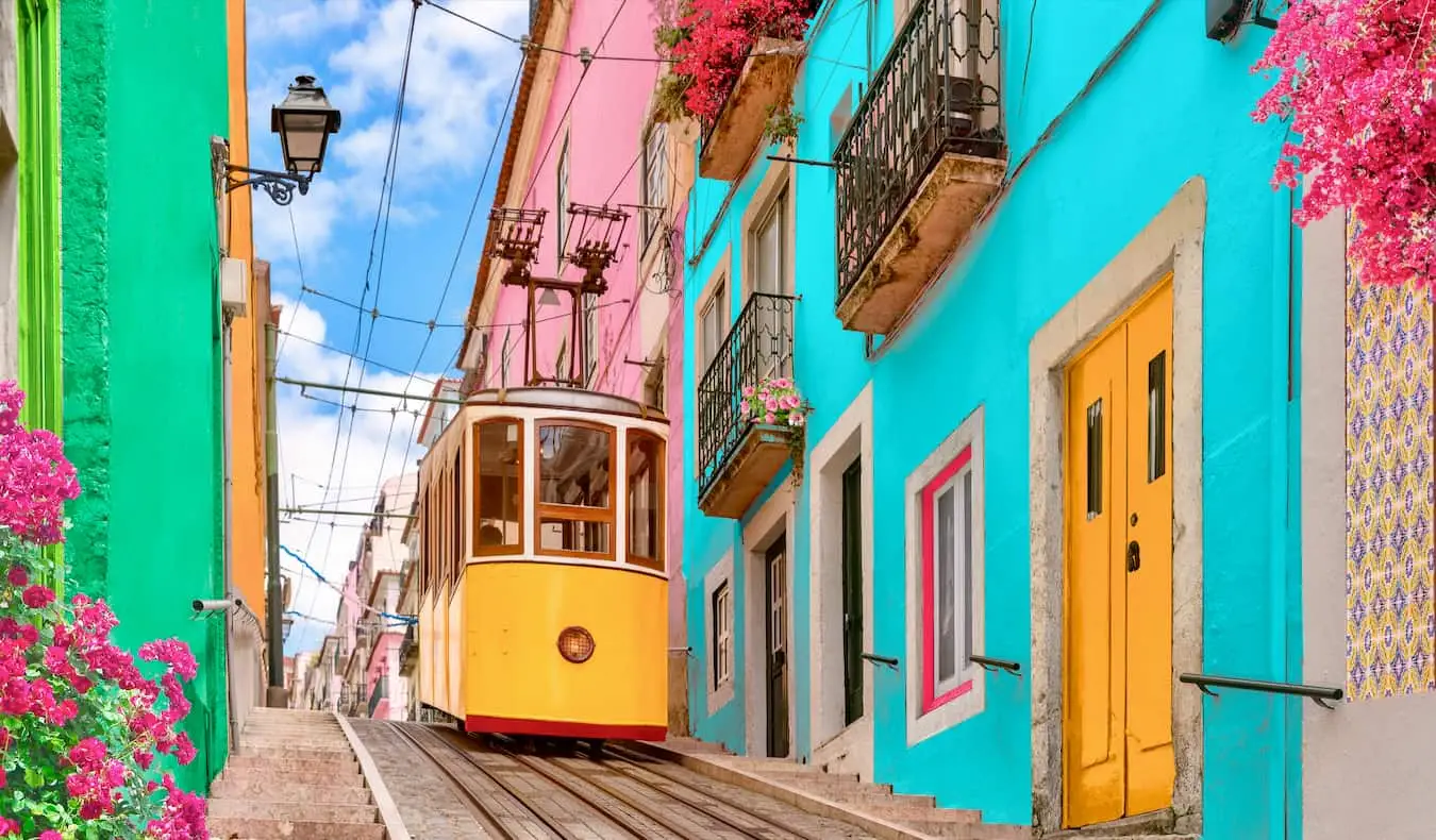 Een smal straatje met felle kleuren en een oude tram die de heuvel op gaat in Lissabon, Portugal