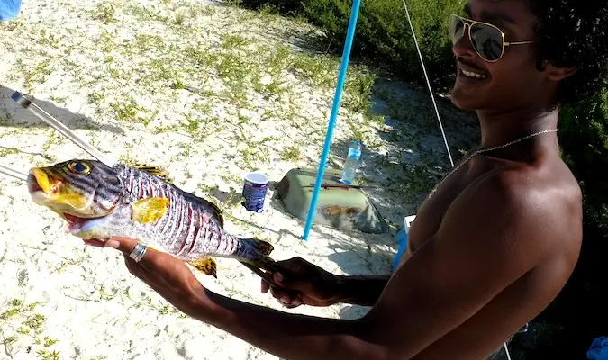 Uomo maldiviano che indossa occhiali da sole con in mano un grande pesce appena pescato.