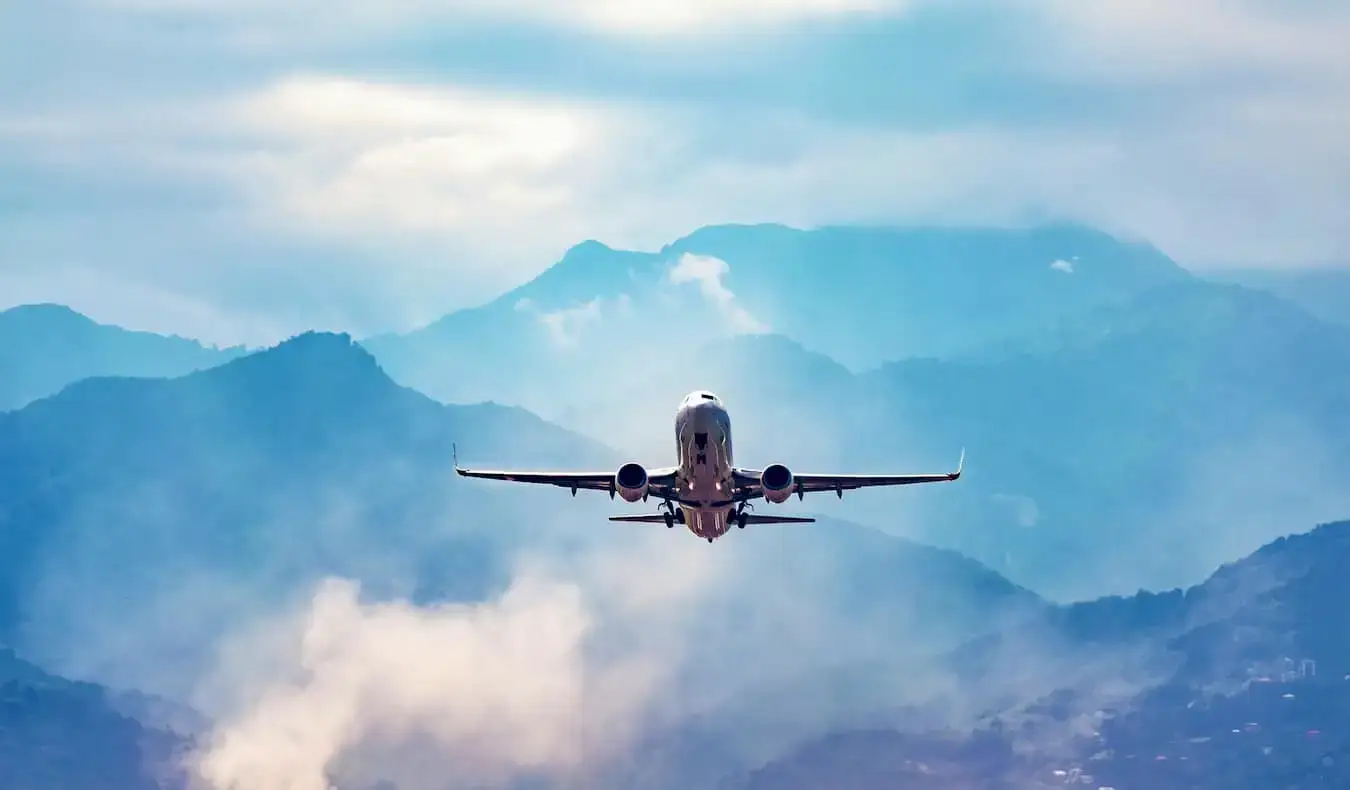 En ensam kommersiell jet som flyger genom en klarblå himmel med berg i fjärran