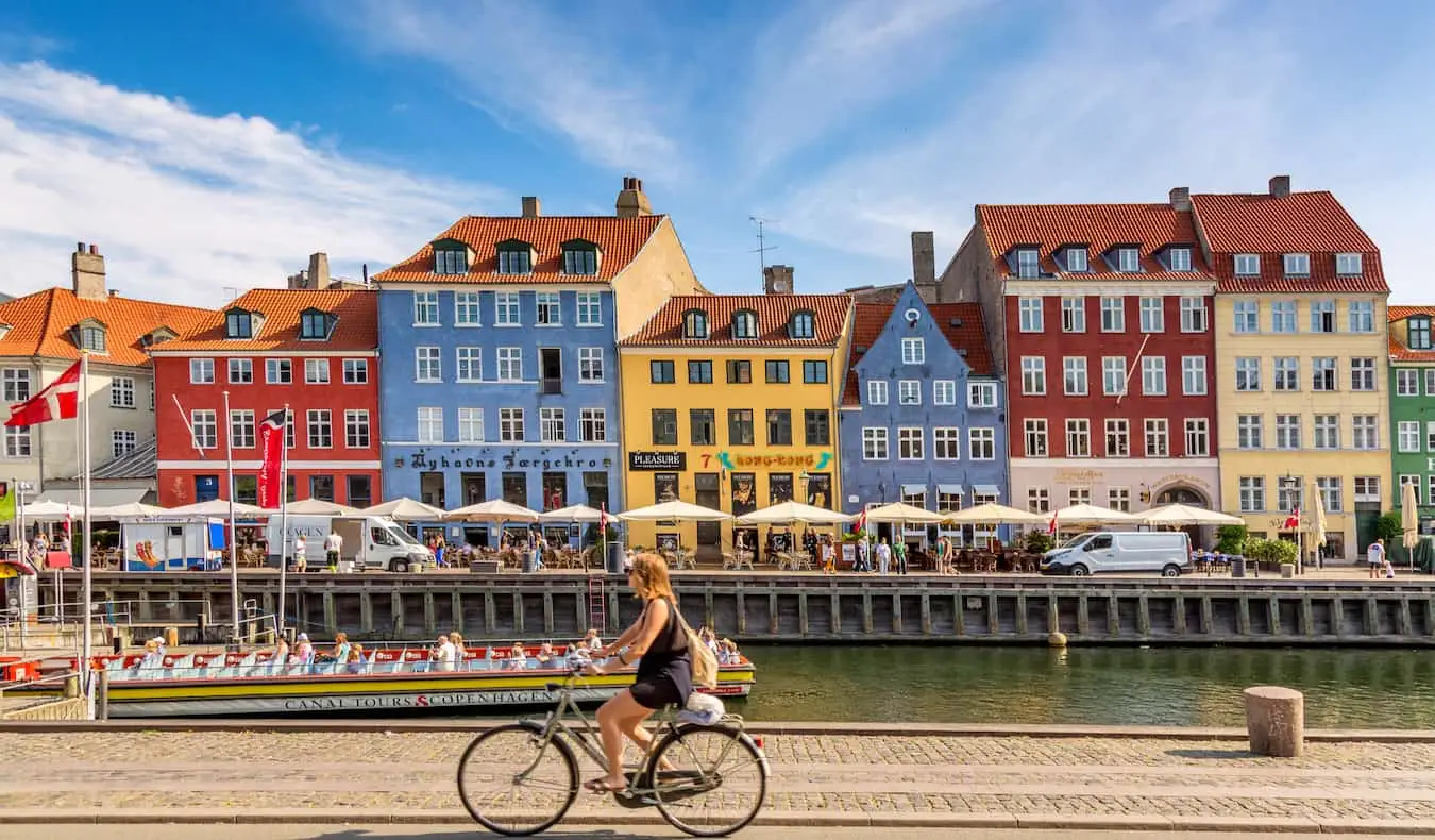 Os edifícios coloridos de Copenhague ao longo da água enquanto alguém passa de bicicleta